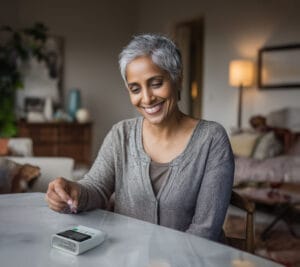 Adult woman performing an at-home A1C test using the OBM rapid A1C test kit in her living room