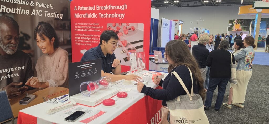 Orange Biomed team demonstrating A1C testing technology to attendees at the ADCES 2026 exhibition booth